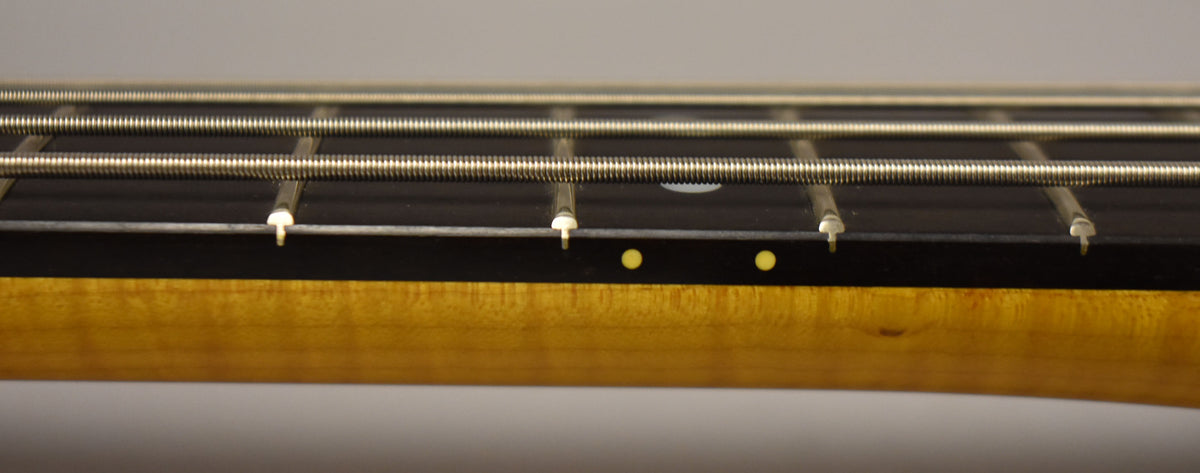 Close-up of the bass neck from the side, showing the dark fretboard, four strings, and two yellow dot markers on the side.