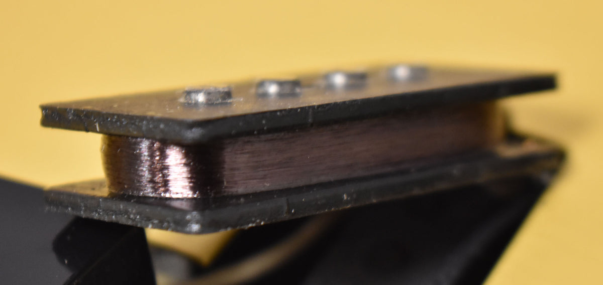 Close-up of a black P-style pickup, showing the copper wire coil between two black plastic plates and four silver pole pieces.