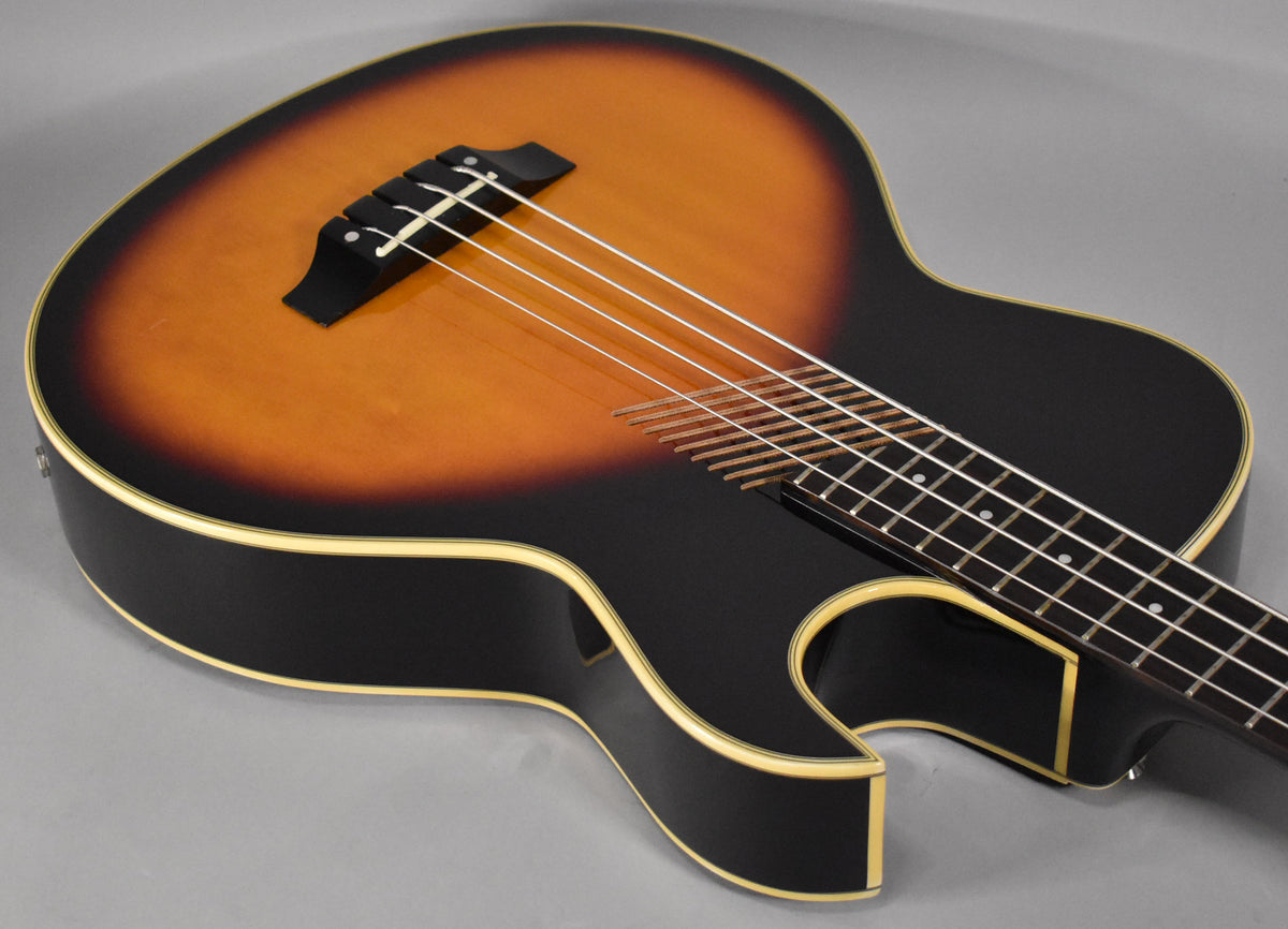 Close-up of the sunburst hollowbody bass, angled from the upper left, showing the bridge, strings, and part of the fretboard.