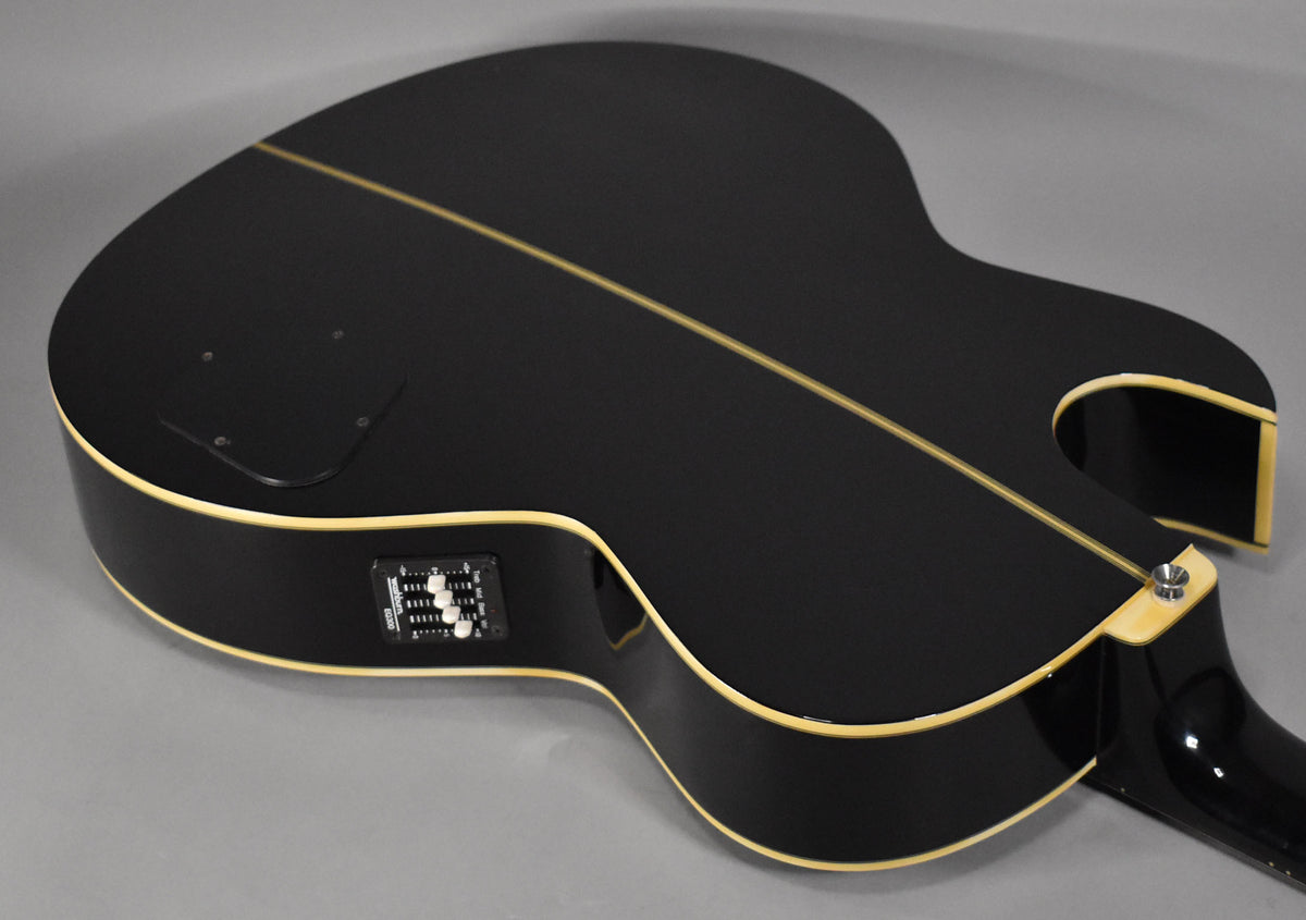 The black hollowbody bass is angled to show its back, with a light stripe down the center and cream binding.