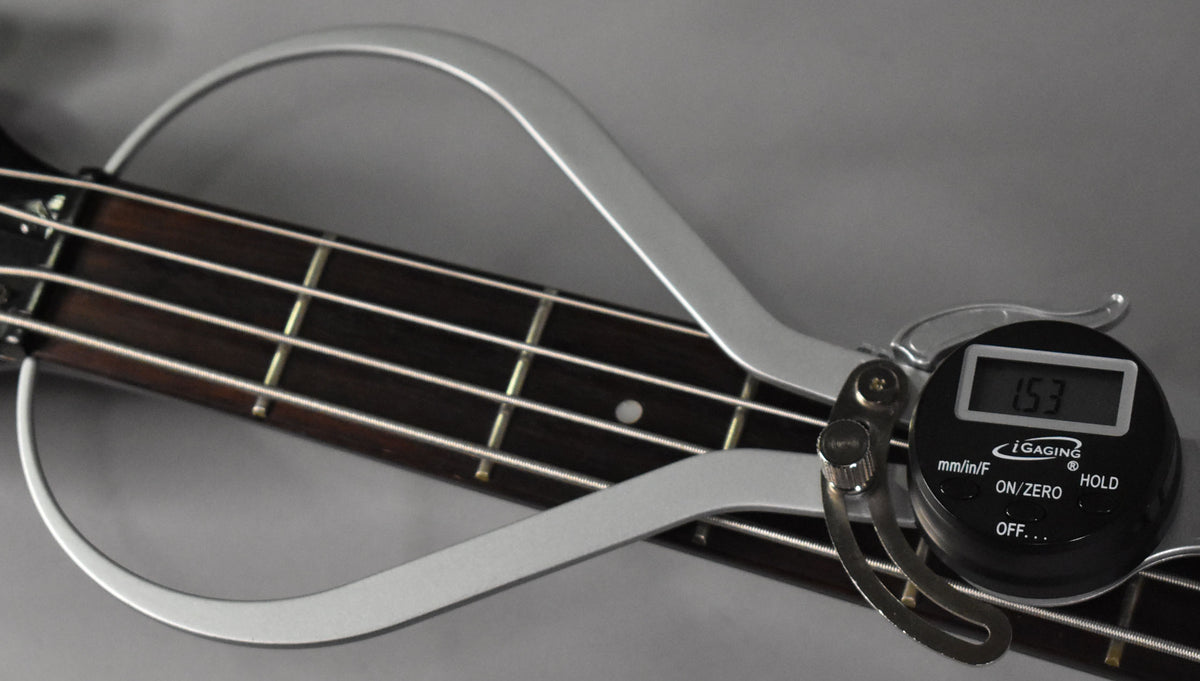 A digital caliper measures the dark rosewood fretboard of the bass, showing a reading of 1.53.