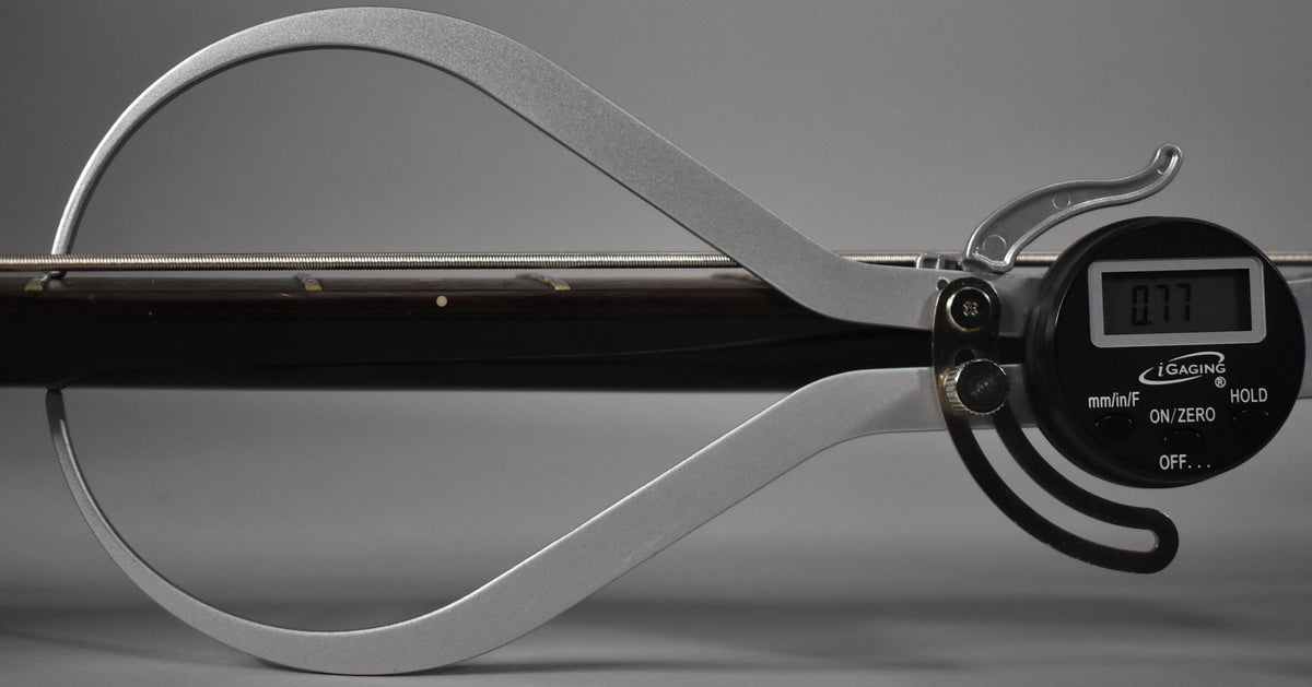 A digital caliper measures the bass neck and strings, displaying "0.77" on its screen.