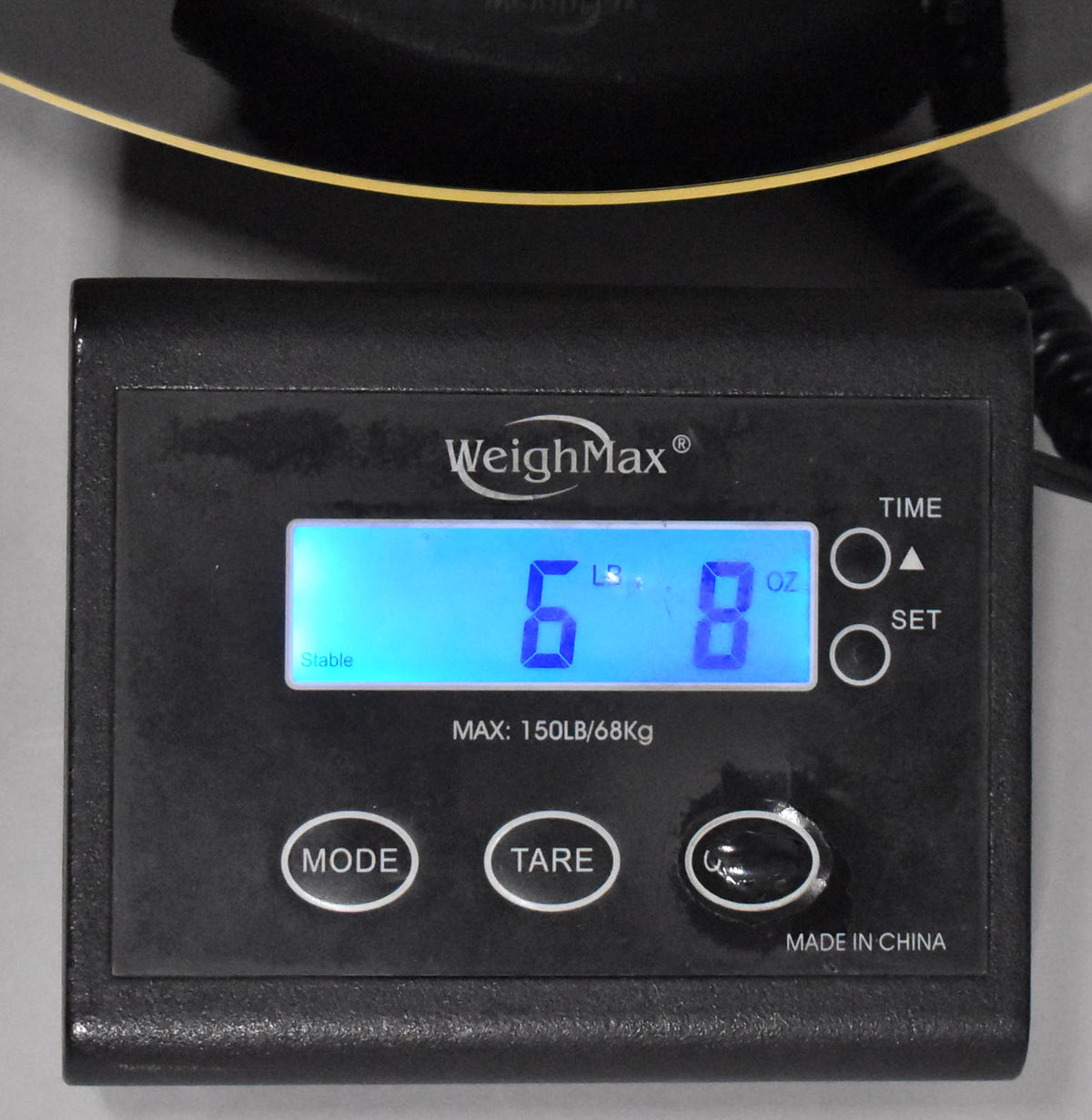 Close-up of a black digital scale displaying "6 LBS 8 OZ" in blue, with a sunburst bass body partially visible above.
