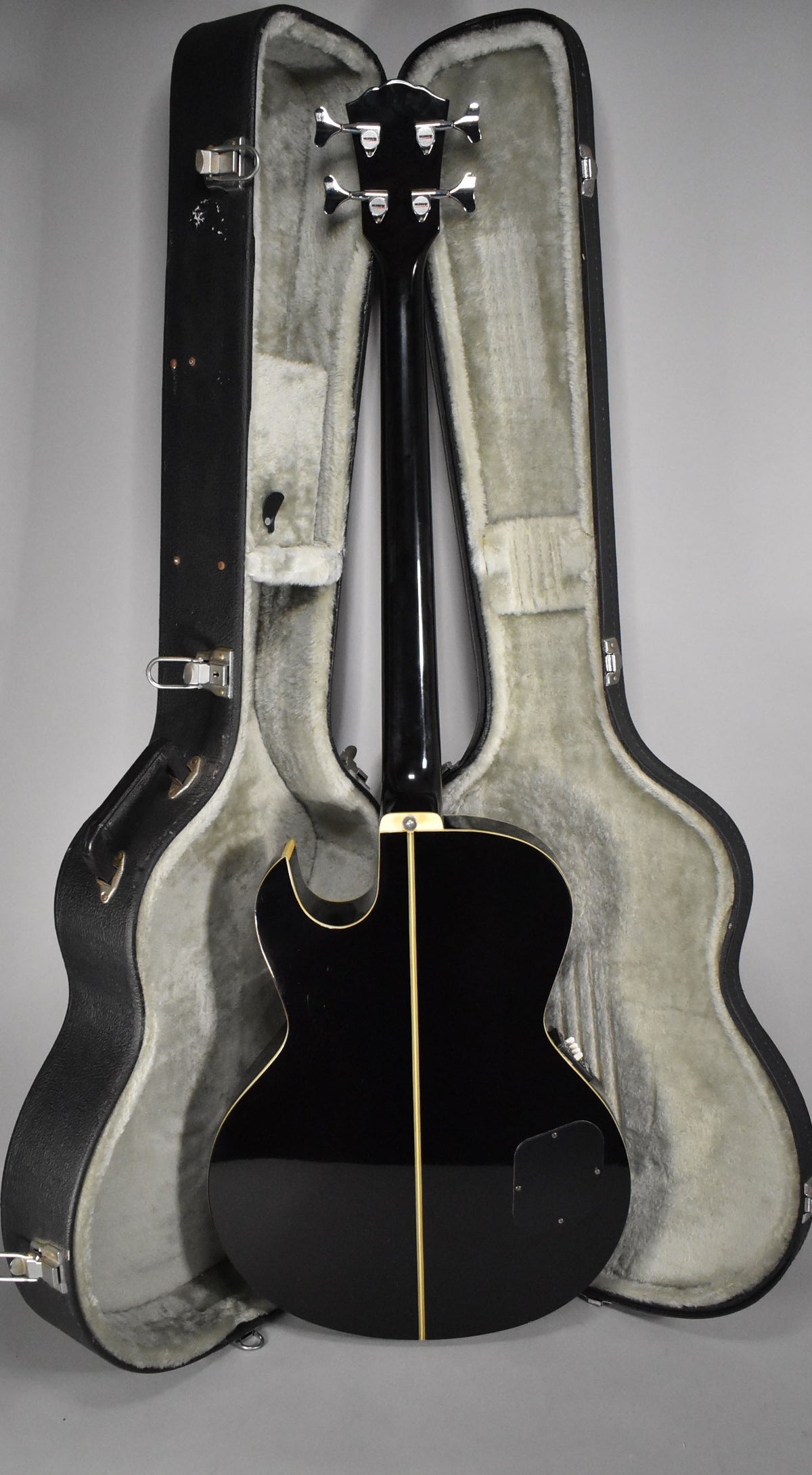 The bass is seen from the back, its glossy black finish with cream binding and center stripe reflecting light, resting in its open case.
