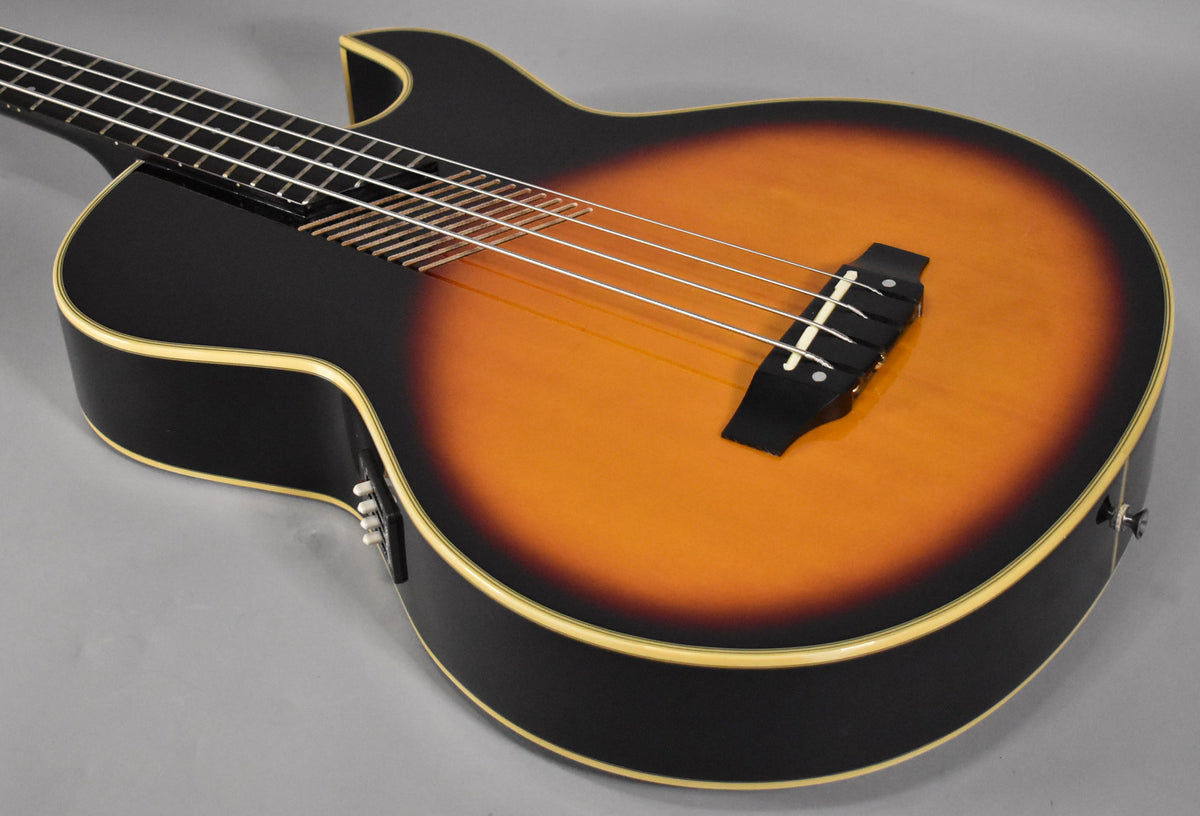 Close-up of the sunburst acoustic bass body, showing the bridge, soundhole, and white binding, with control knobs on the upper bout.