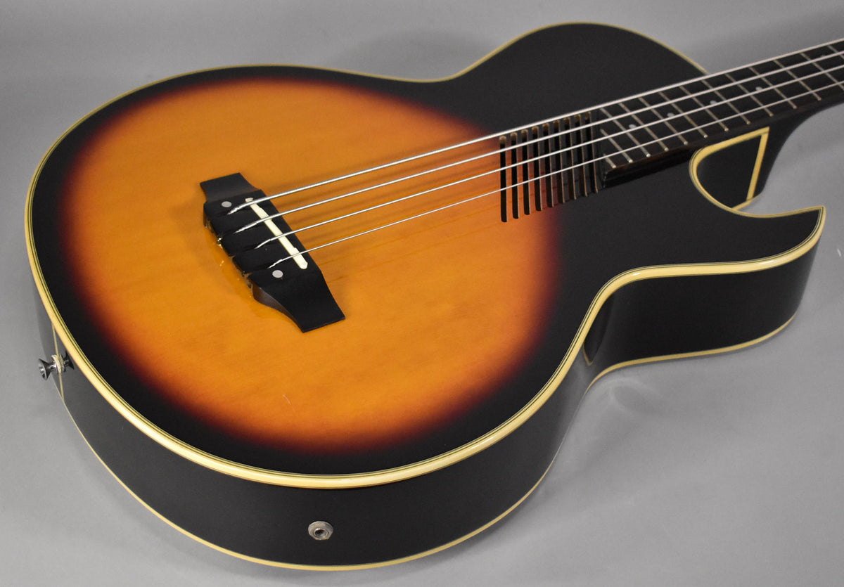 The sunburst hollowbody bass is angled down from the left, showing the black body, light binding, and the bridge with four strings.