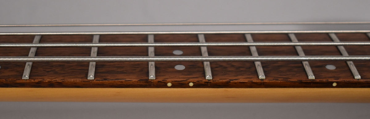Close-up of the bass fretboard, showing dark wood, metal frets, white dot inlays, and light side dots on the neck.