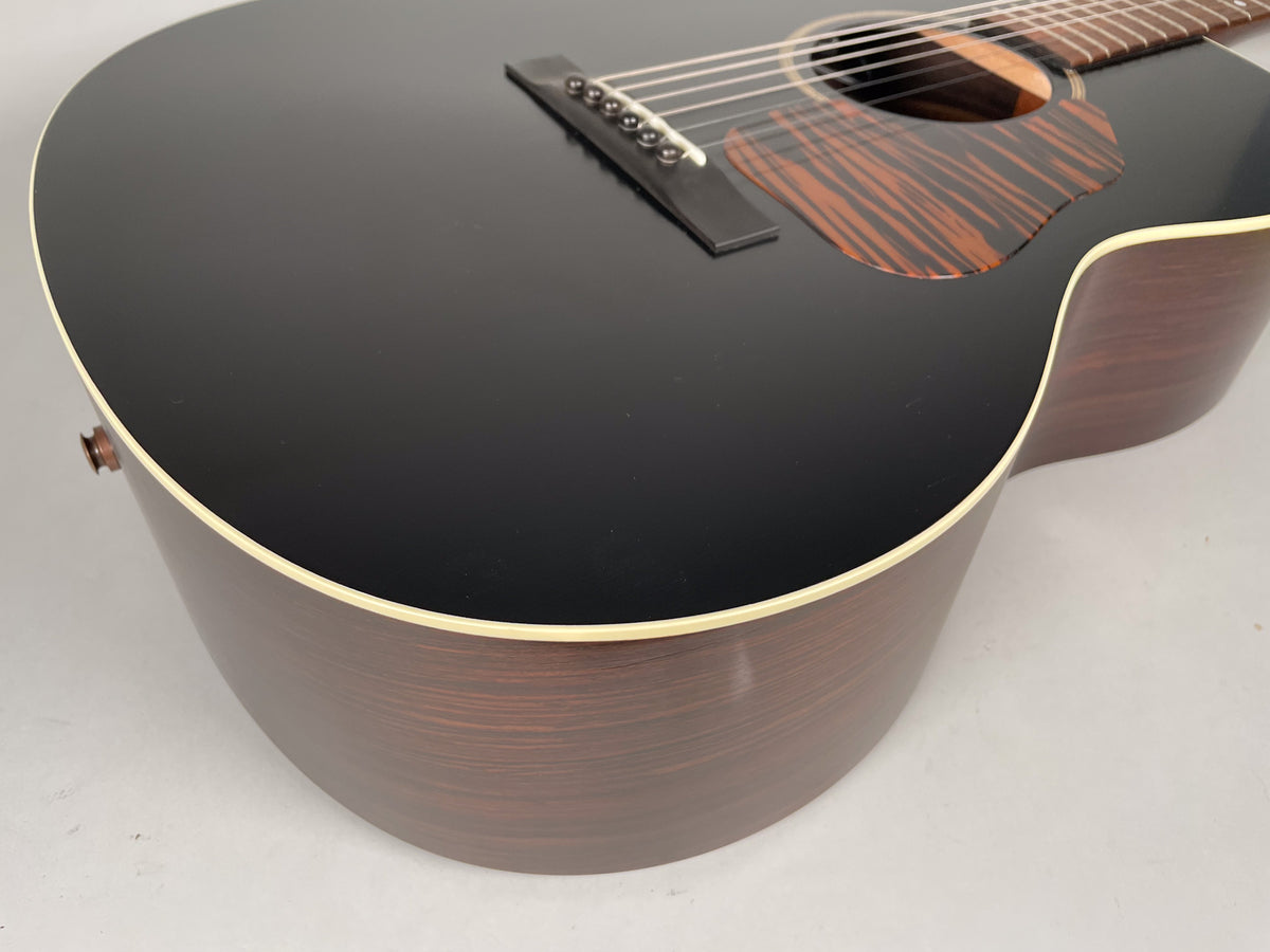 Close-up of a black acoustic guitar's body, showing the dark brown sides, cream binding, and a striped brown pickguard.