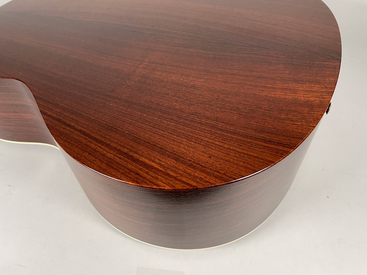 The guitar's dark reddish-brown back and side, with visible wood grain, curves from the lower bout to the waist.