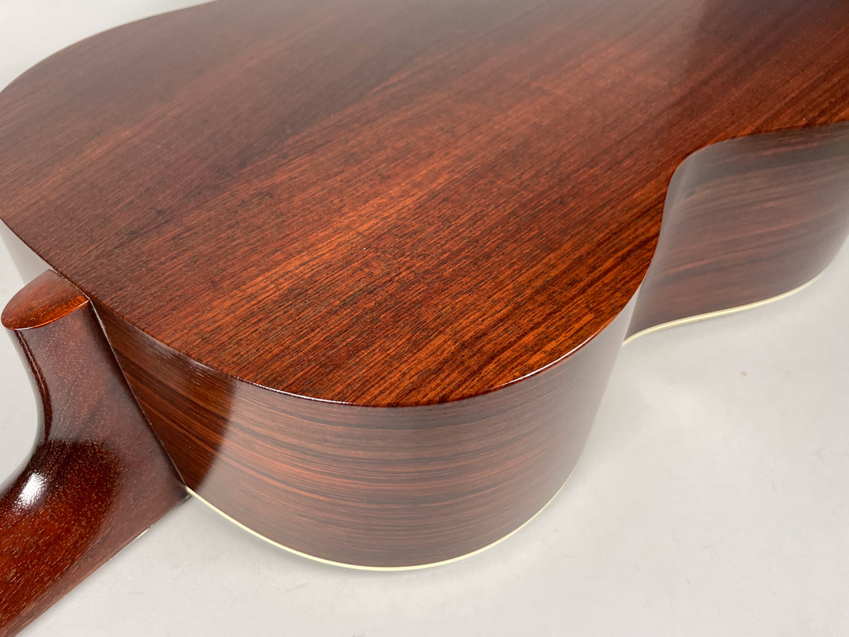 The acoustic guitar's dark reddish-brown back and side are visible, with a glossy finish and light binding along the edge.