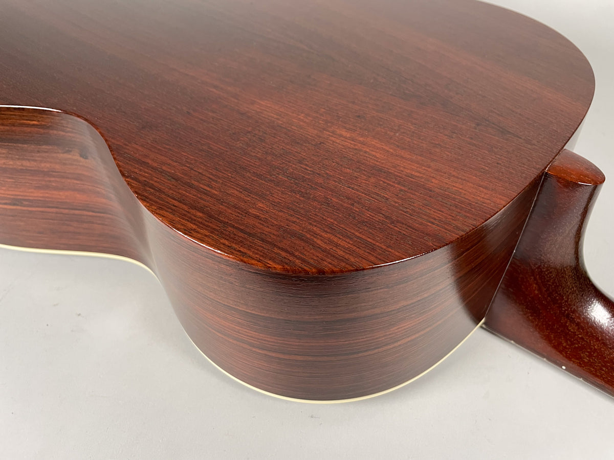 The guitar's dark reddish-brown back and side are visible from the lower bout, with light binding and a glossy finish.