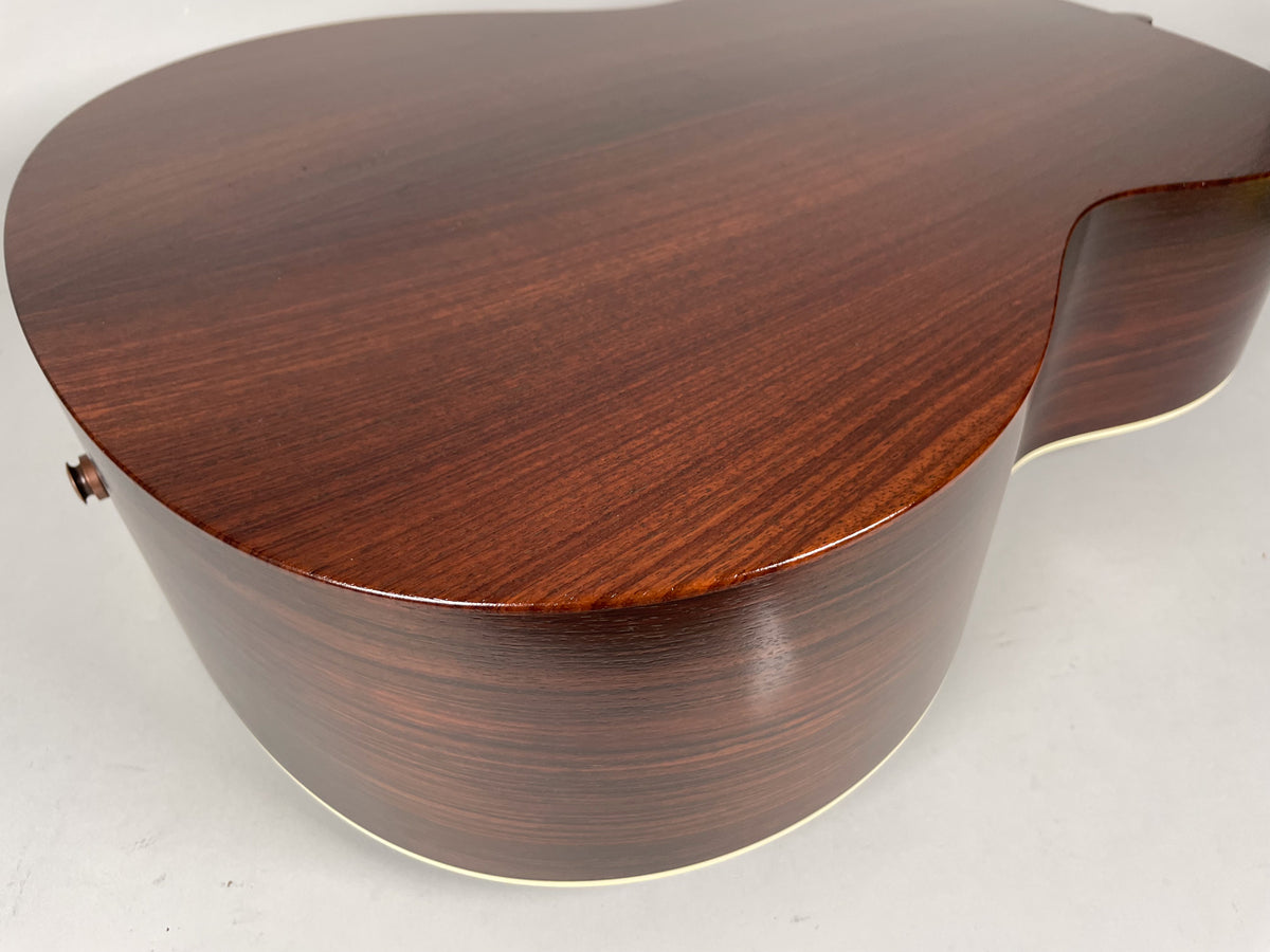 The guitar's dark brown back and side are visible from an overhead angle, showing the wood grain and cream binding.