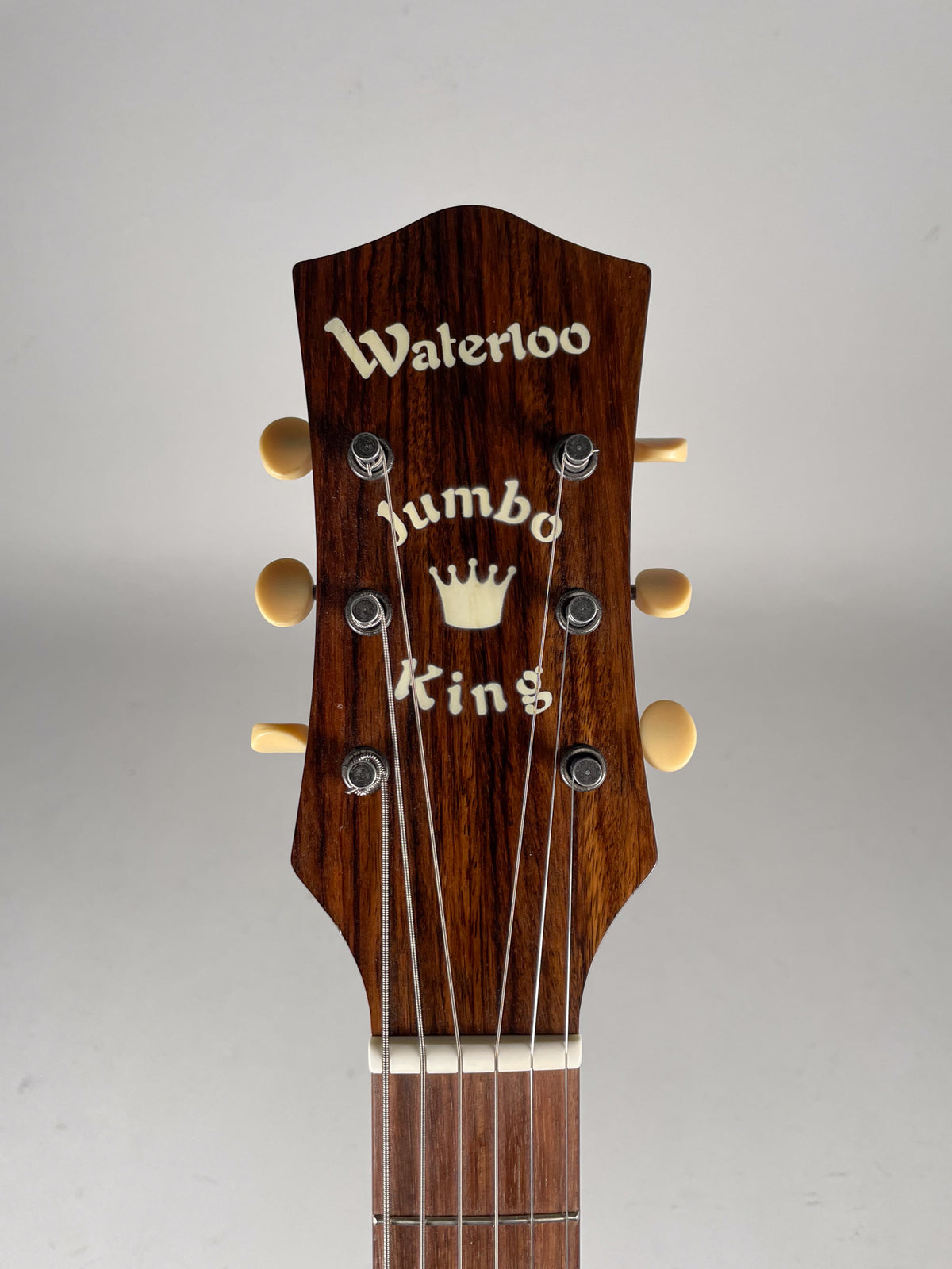 Close-up of the dark brown woodgrain headstock with ivory tuning pegs, showing the top of the fretboard and six strings.