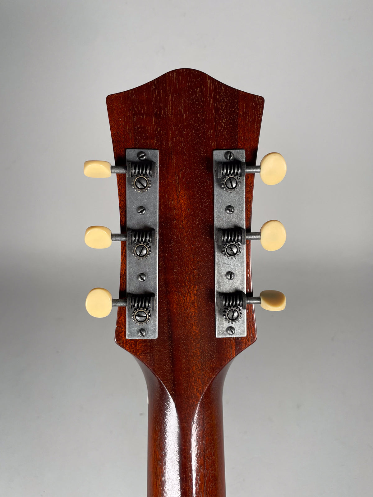 Rear view of the guitar's headstock and upper neck, showing six cream-colored tuning pegs on two weathered metal strips.