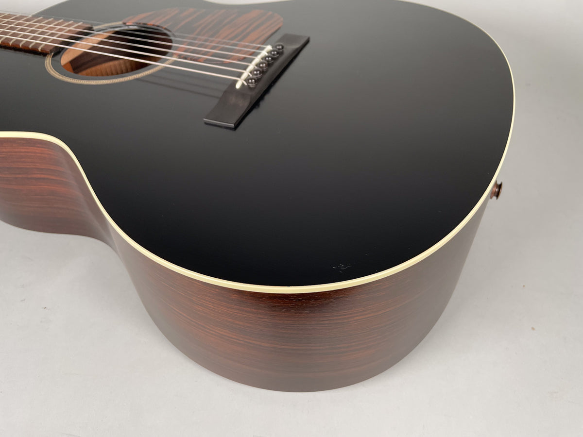 The acoustic guitar's black top and dark wood sides are visible from a low angle, showing a pickguard and bridge.