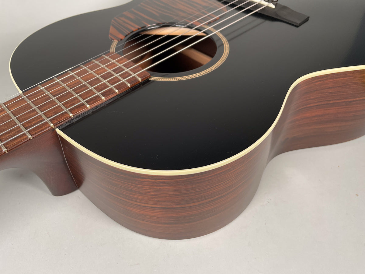 The acoustic guitar's glossy black top and dark brown sides are framed from the lower bout, showing the fretboard and soundhole.