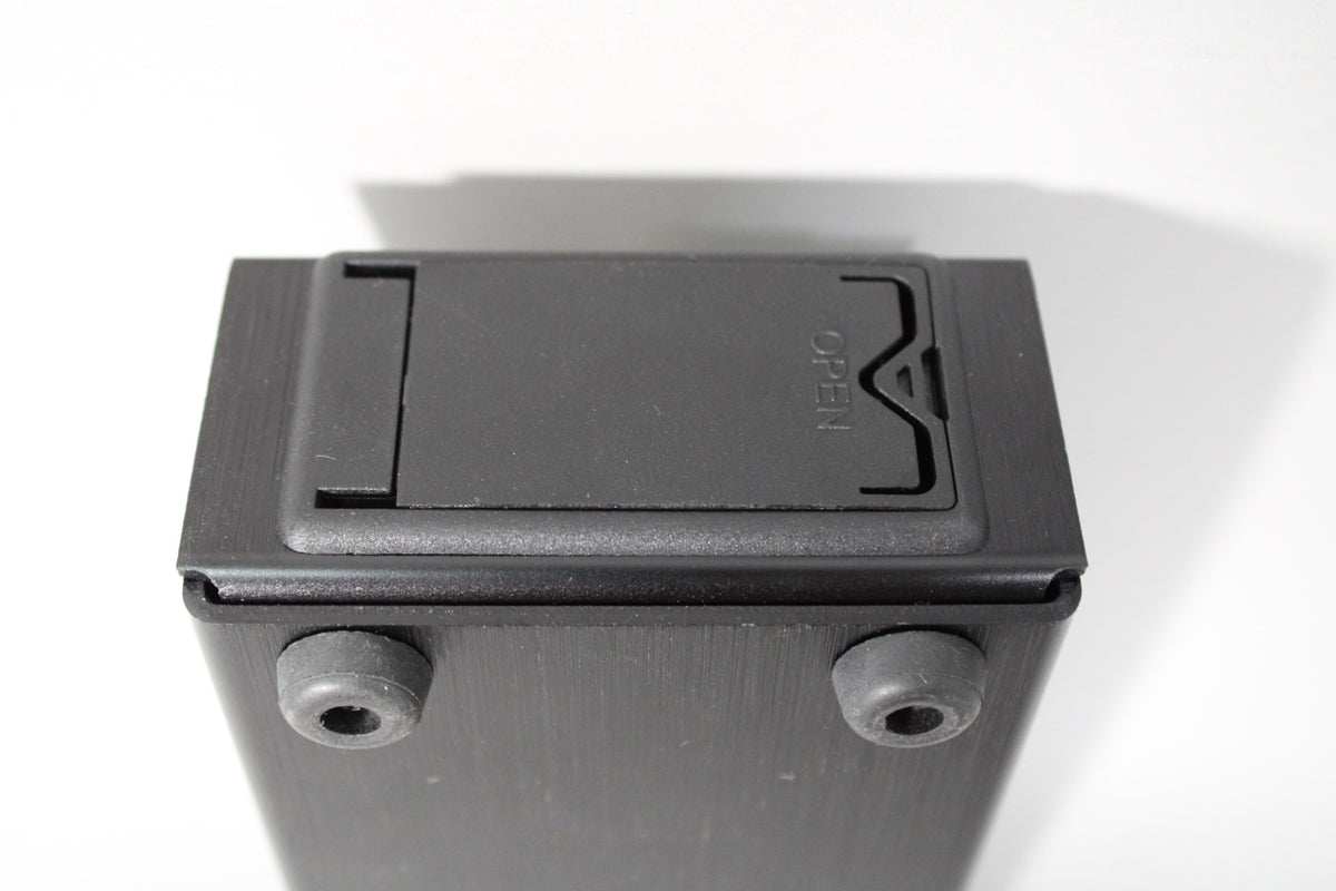 The black pedal is seen from the bottom, revealing a battery compartment with "OPEN" molded into the cover and two rubber feet.