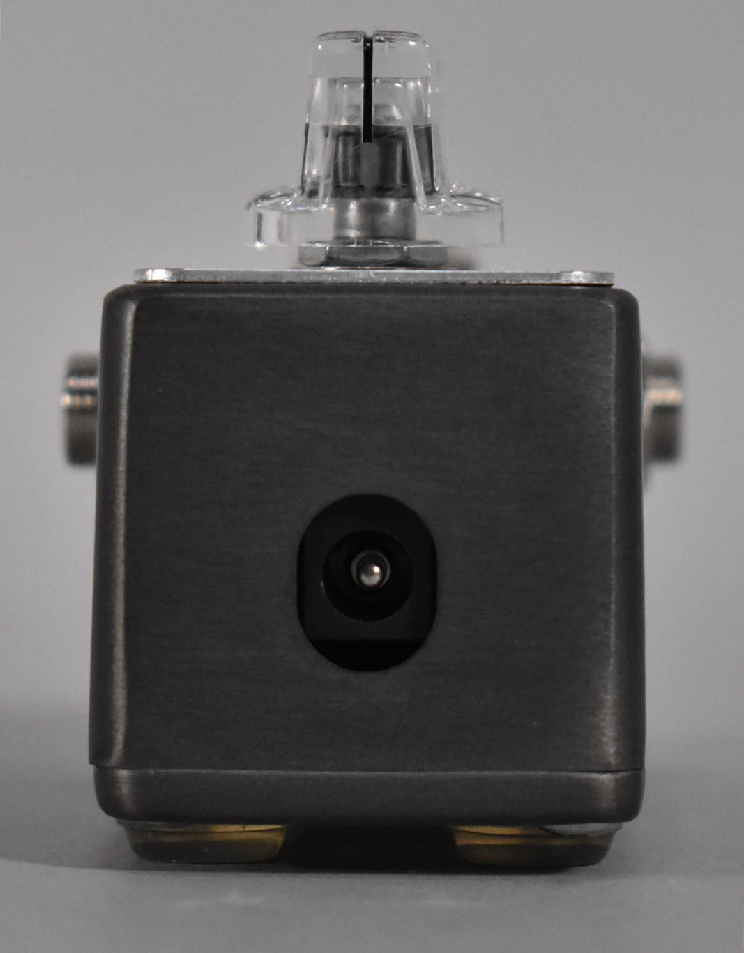 Front view of the dark gray mini pedal, showing a clear plastic knob on top and a power input jack centered on the front face.