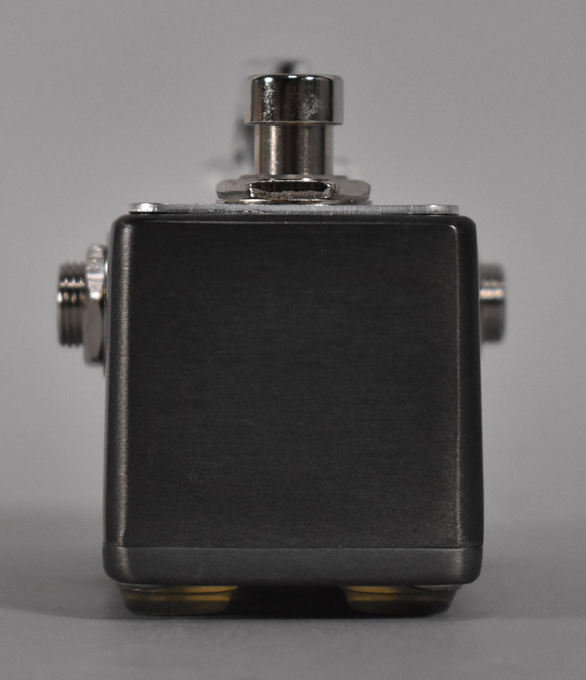 The mini pedal is shown from the front, revealing its dark gray, brushed metal finish, a chrome footswitch, and two gold feet.