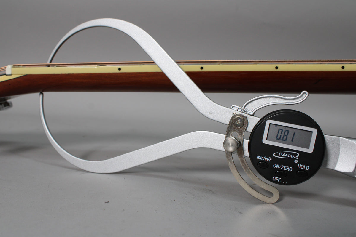 A digital caliper measures the guitar's dark brown neck, showing a 0.81 reading on its black display.
