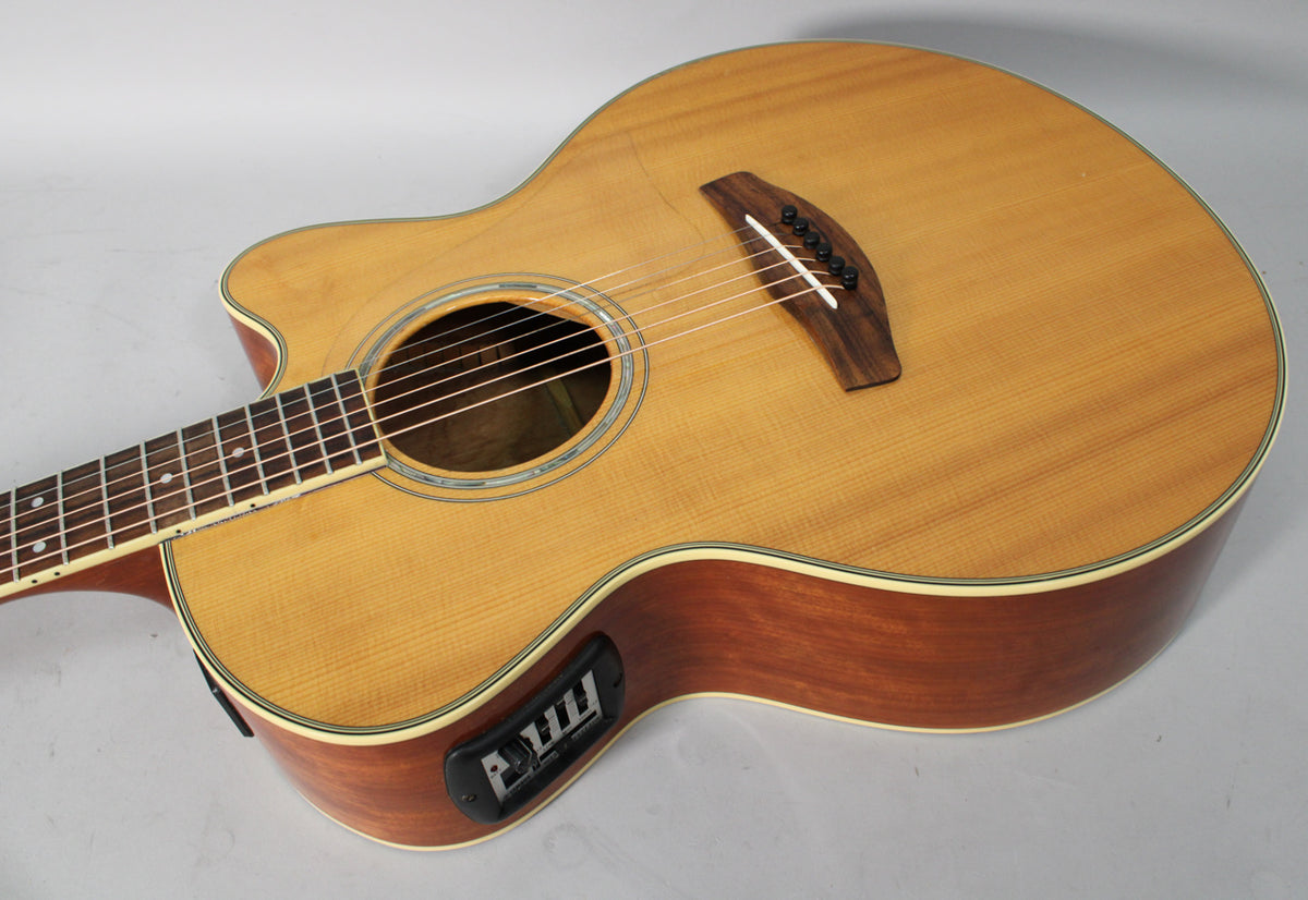 Acoustic-electric guitar, light wood top, dark wood sides, cutaway body, and visible black preamp controls on the upper bout.