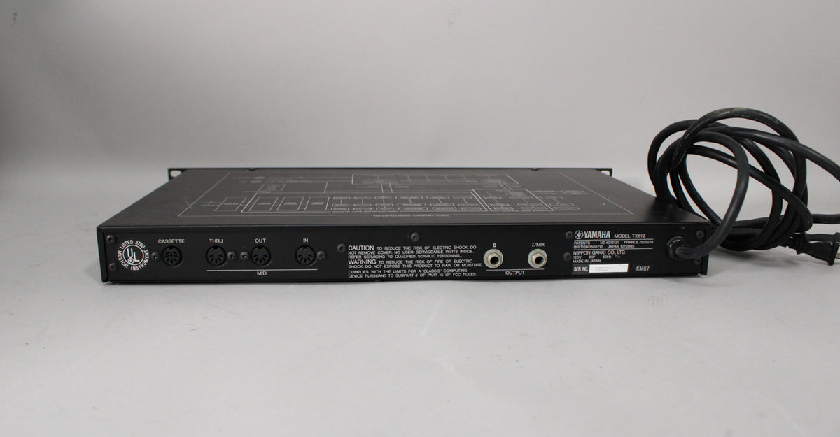 The black rackmount unit is seen from the rear, showing MIDI In/Thru/Out, Cassette, and two Output jacks, plus a coiled power cord.