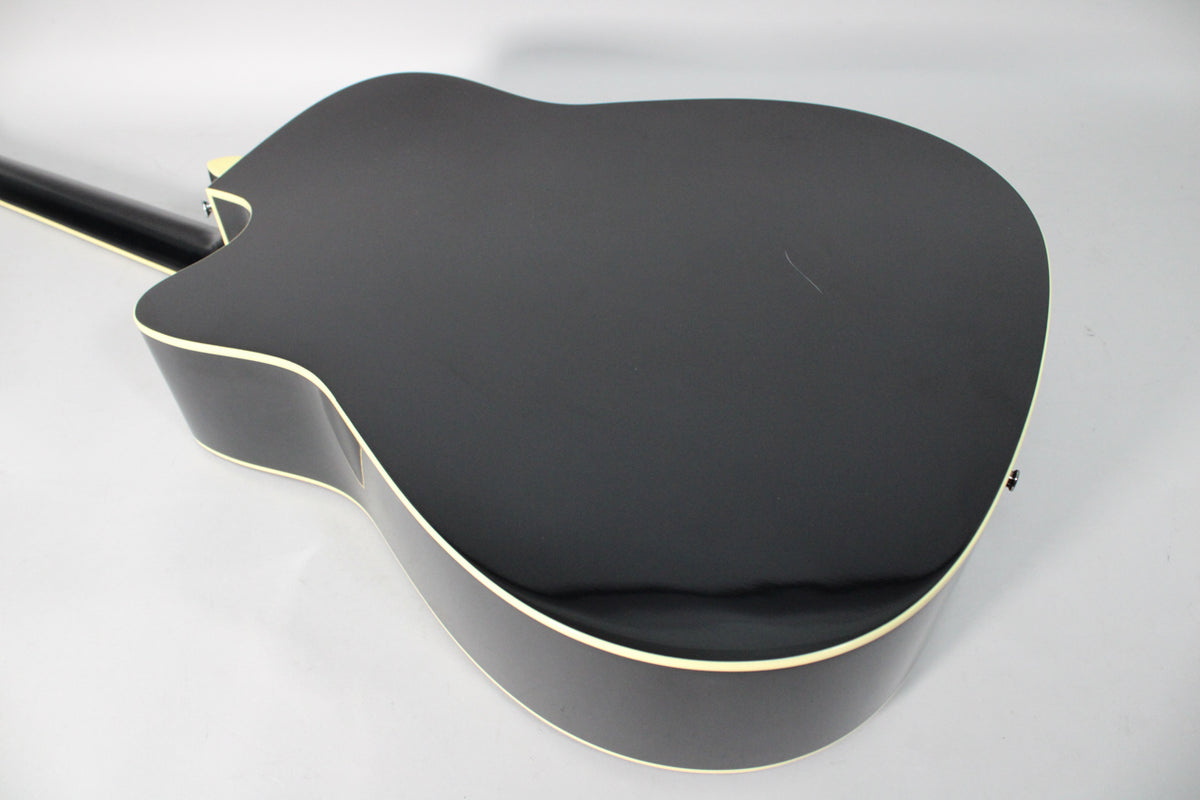 The glossy black acoustic guitar body is angled, showing the back and side with cream binding and a visible scratch near the center.