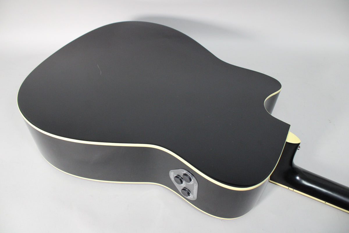 The black matte acoustic guitar's back and sides are visible, with cream binding and two black control knobs on the upper bout.