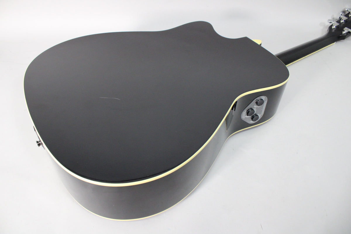 The black acoustic guitar's back and side are visible, with a small scratch on the glossy finish and side-mounted controls.