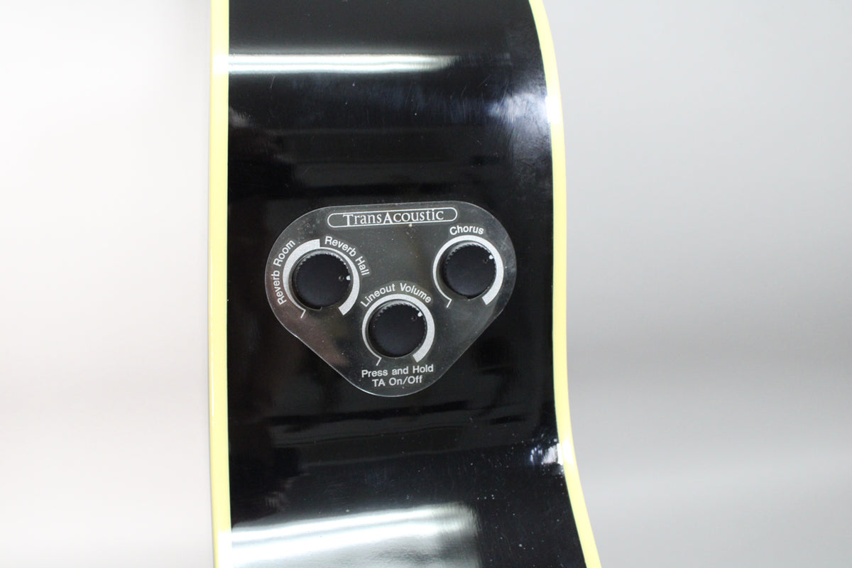 Close-up of the guitar's glossy black side, showing the TransAcoustic control panel with three black knobs for Reverb, Chorus, and Volume.