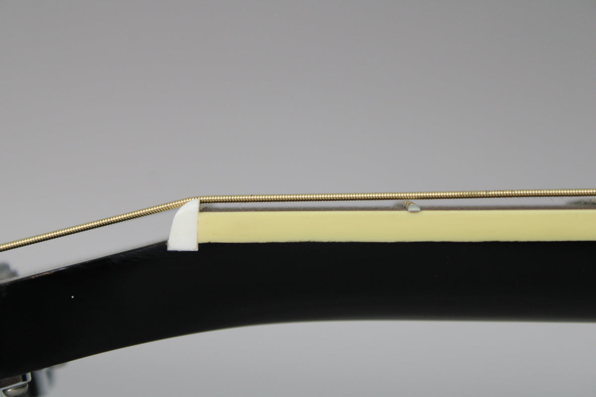 Close-up of the black guitar's headstock, showing the white nut, light-colored fretboard binding, and a small ding on the fretboard.