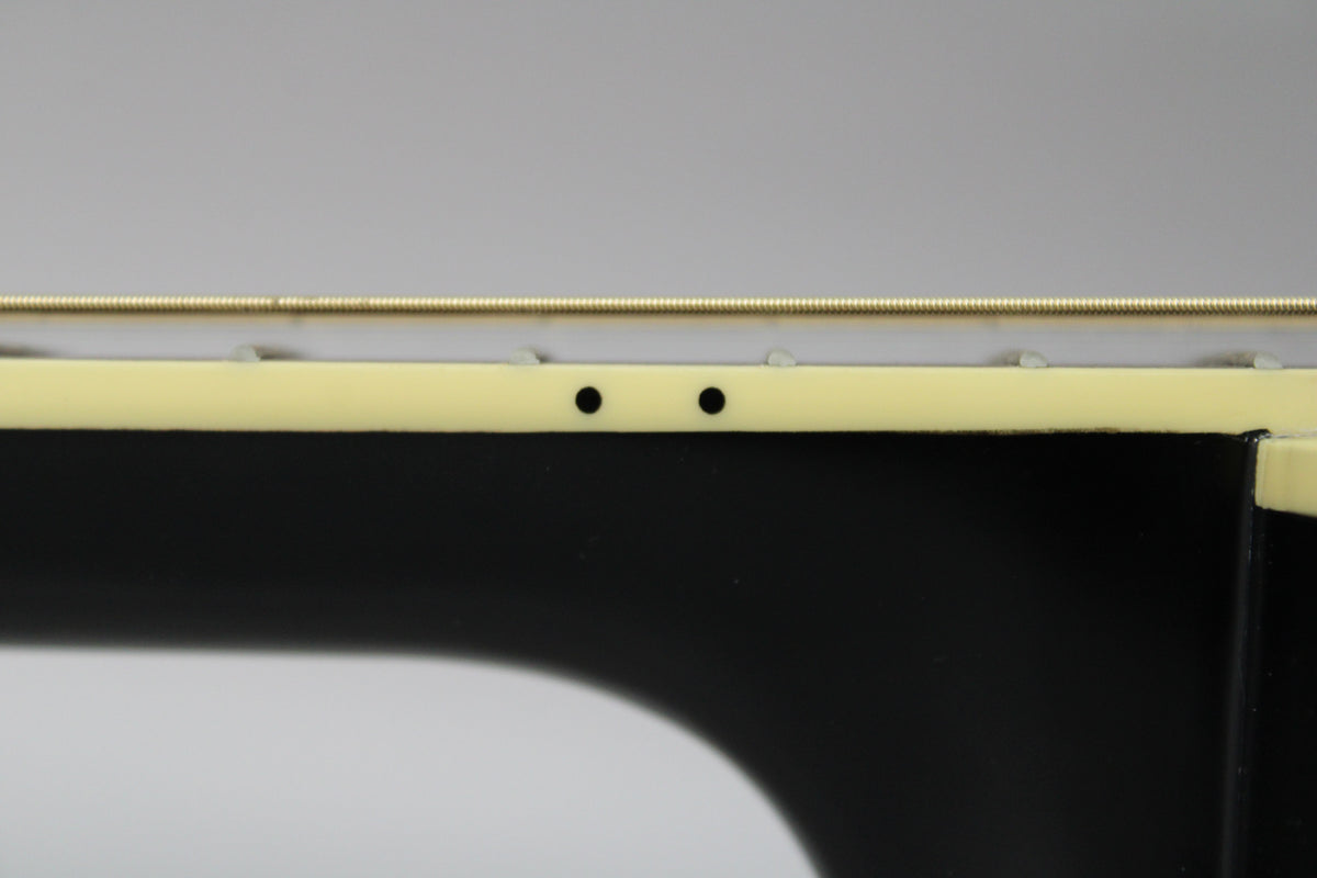 Close-up of the guitar's black body and cream binding, showing two small black control knobs on the upper bout.