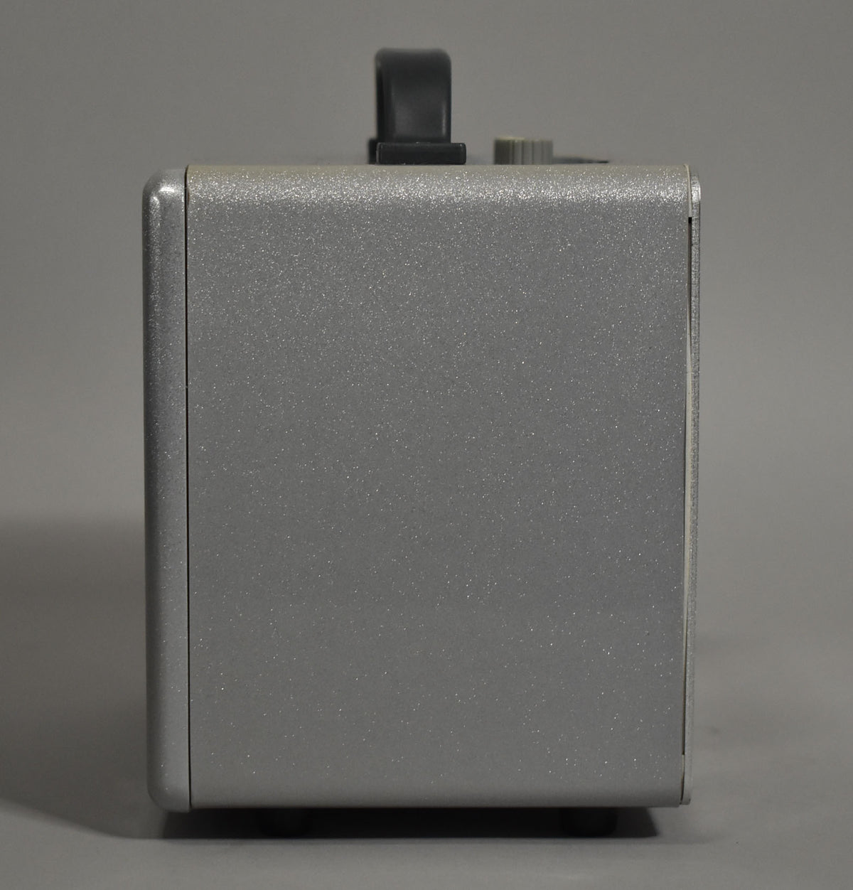 The amp's right side is shown, revealing its speckled silver-gray finish, a black handle, and a gray knob on top.
