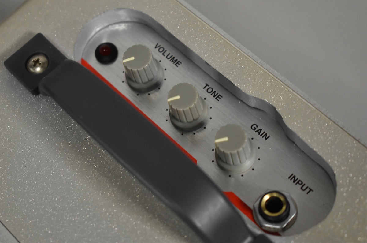 Close-up of the amp's silver control panel, showing a red power light, three grey knobs, and an input jack, with a black handle.