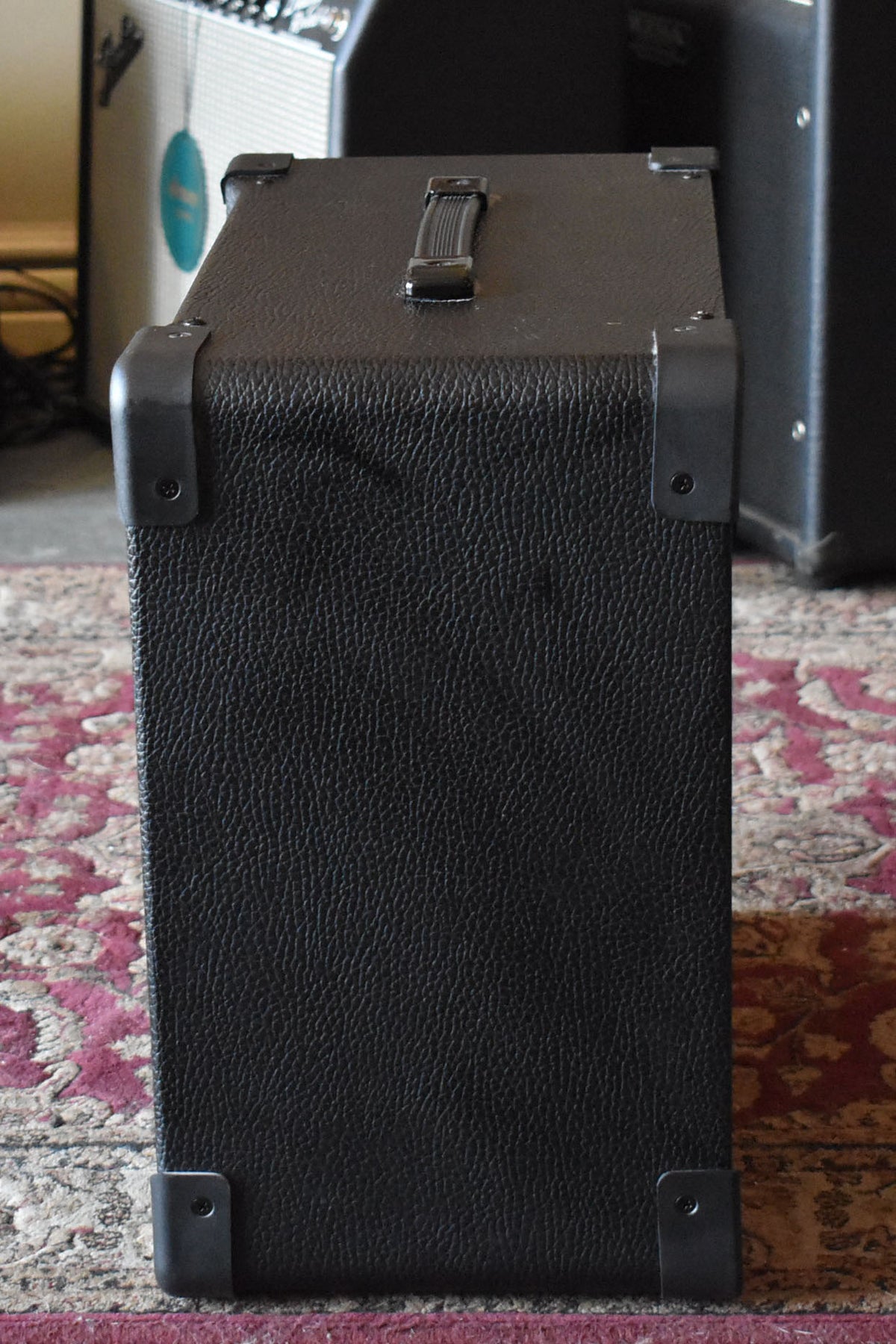 The amp's right side, covered in black Tolex with a textured finish, shows a top handle and four protective corner caps.