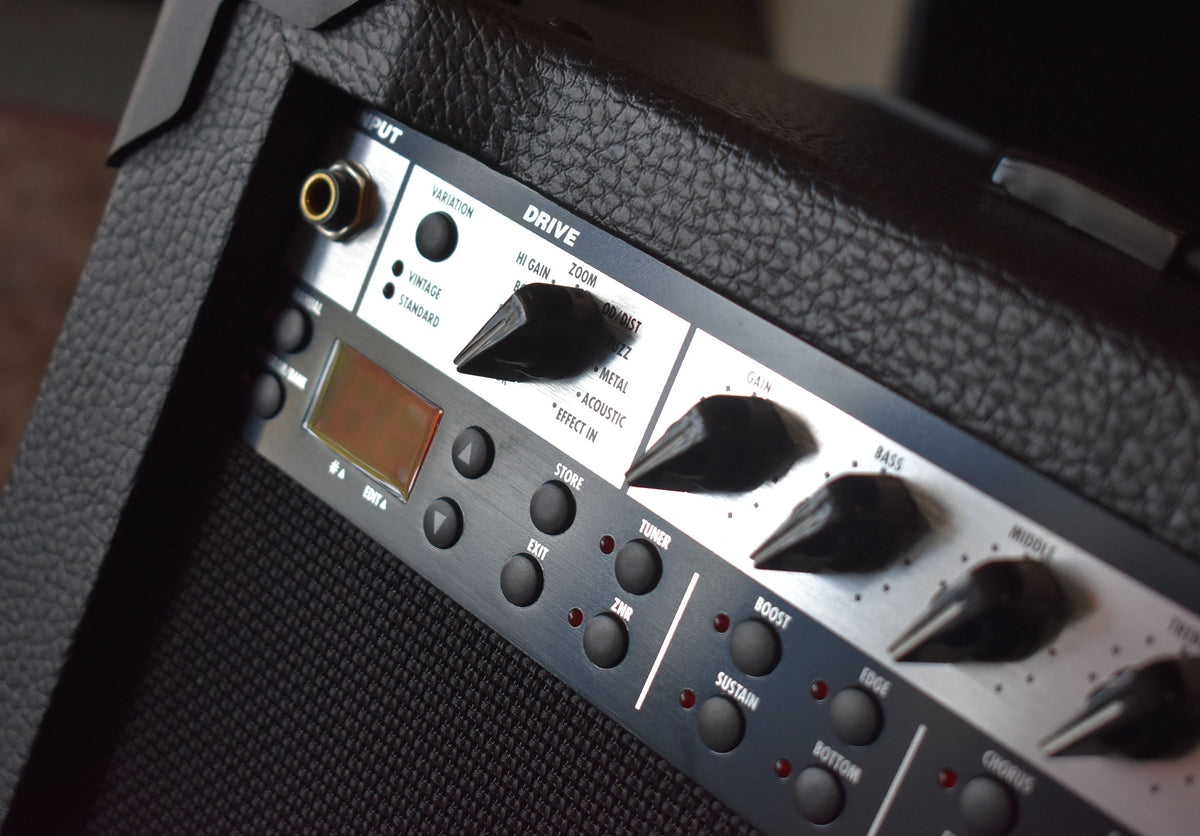 Close-up of the amp's black control panel, showing a gold input jack, an orange LCD, and numerous black knobs and buttons.