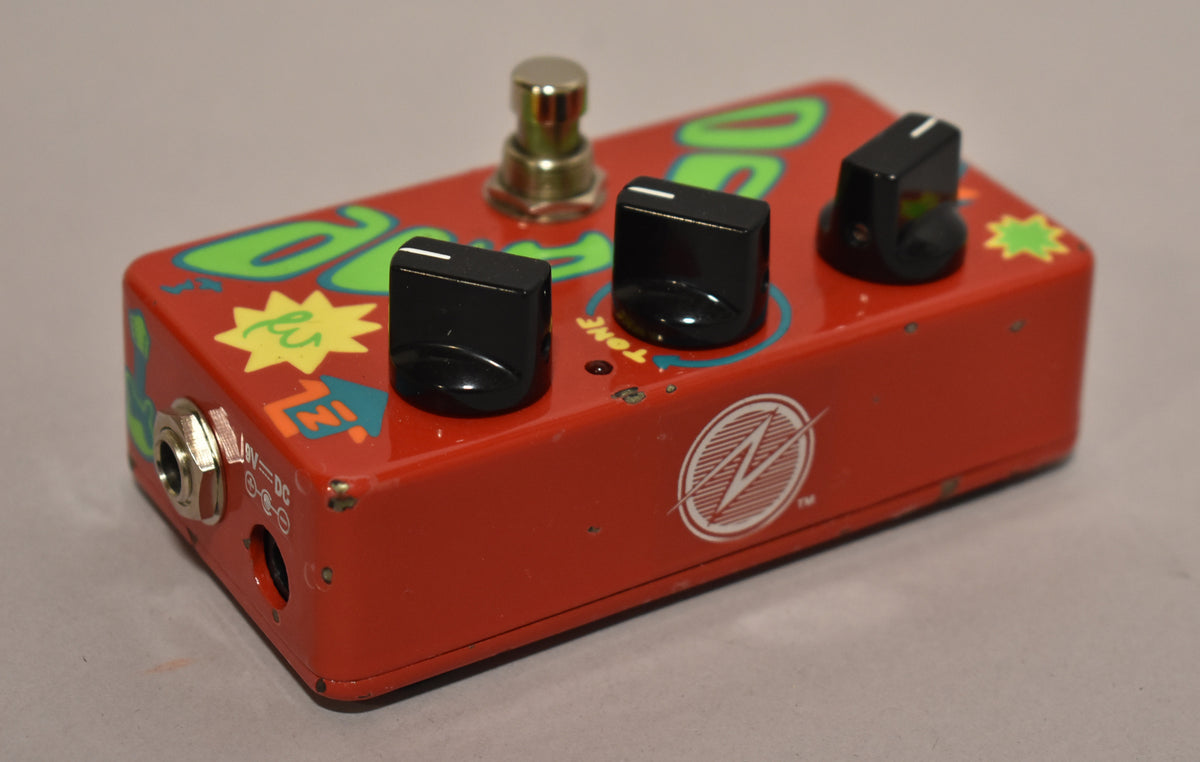 The red pedal, viewed from the front-left, has three black knobs, a silver footswitch, and a hand-painted green and yellow design.