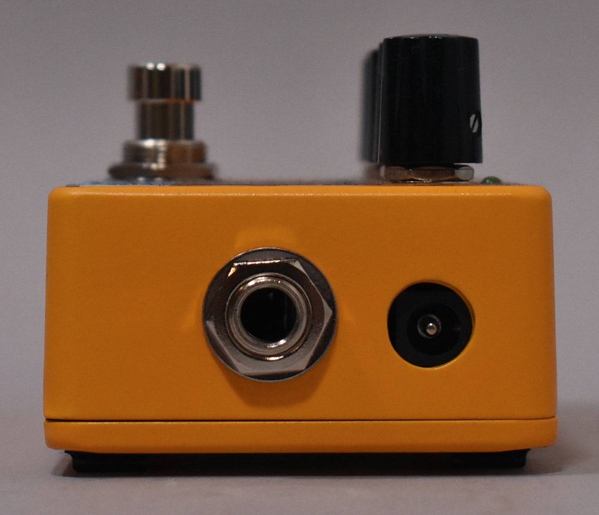 The bright orange pedal's rear shows a chrome input jack and a black power input, with a footswitch and knob visible above.