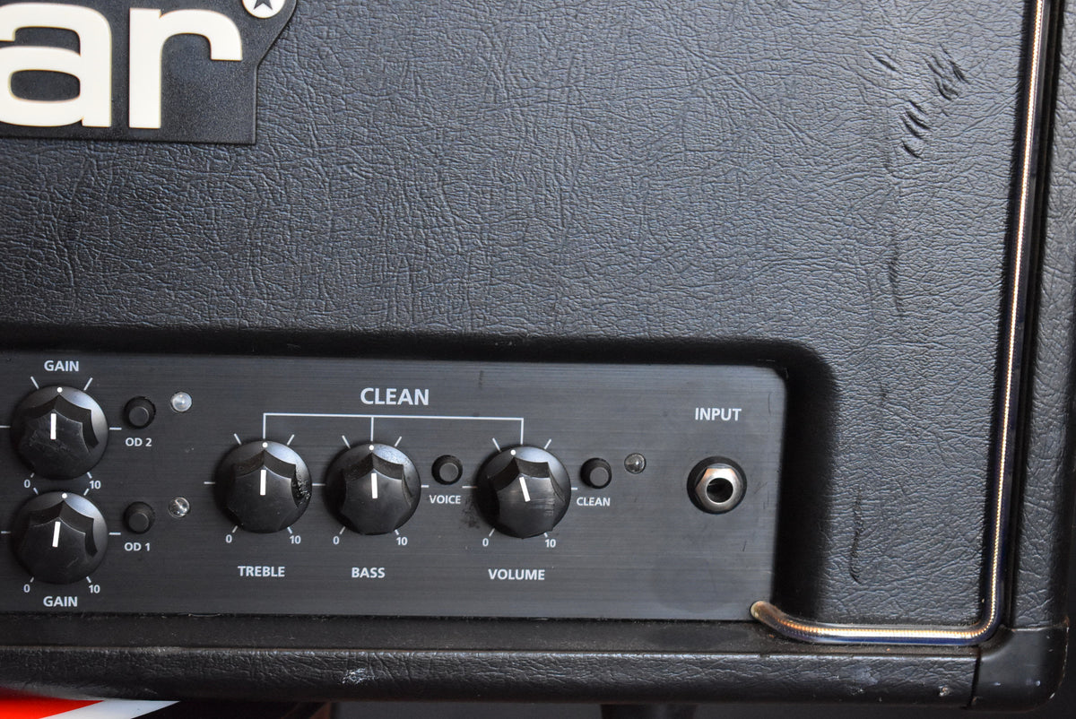 Close-up of the black amp's textured tolex and brushed metal control panel with black knobs, showing some scuffs and wear on the top right.