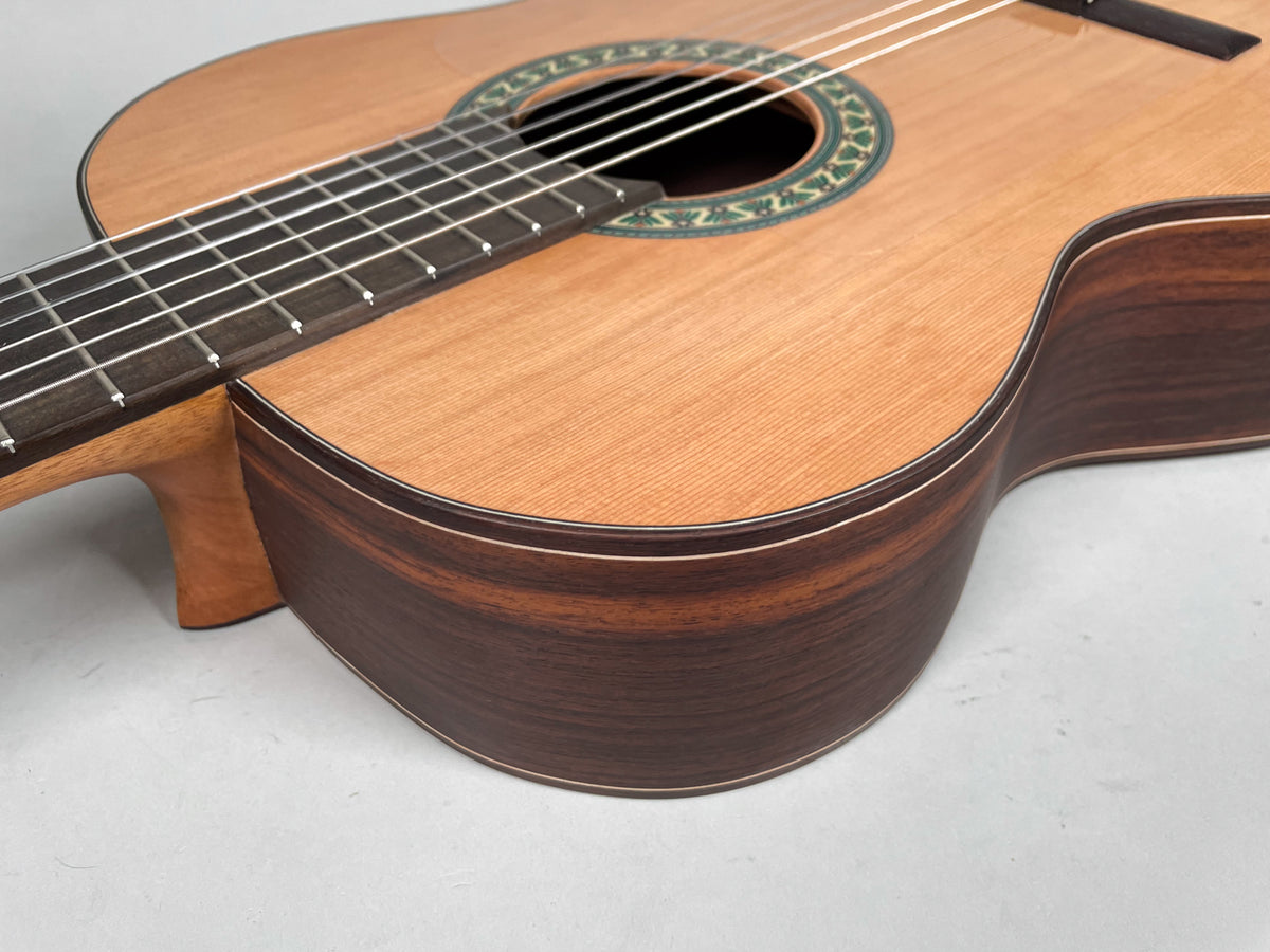 Close-up of the guitar's lower bout and neck heel, showing the light wood top, dark sides, and green-patterned rosette.