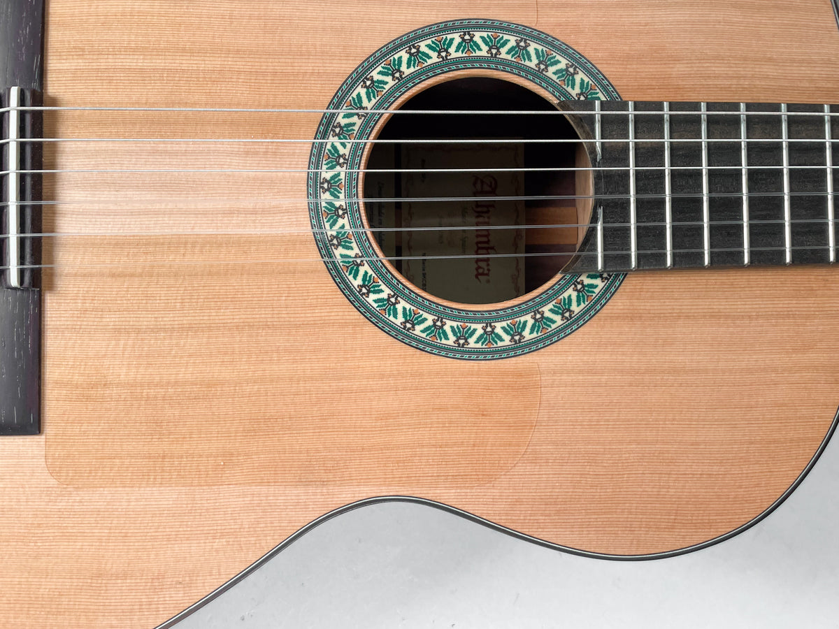 The light wood guitar body is framed from the bridge to the fretboard, showing the ornate green and white rosette.