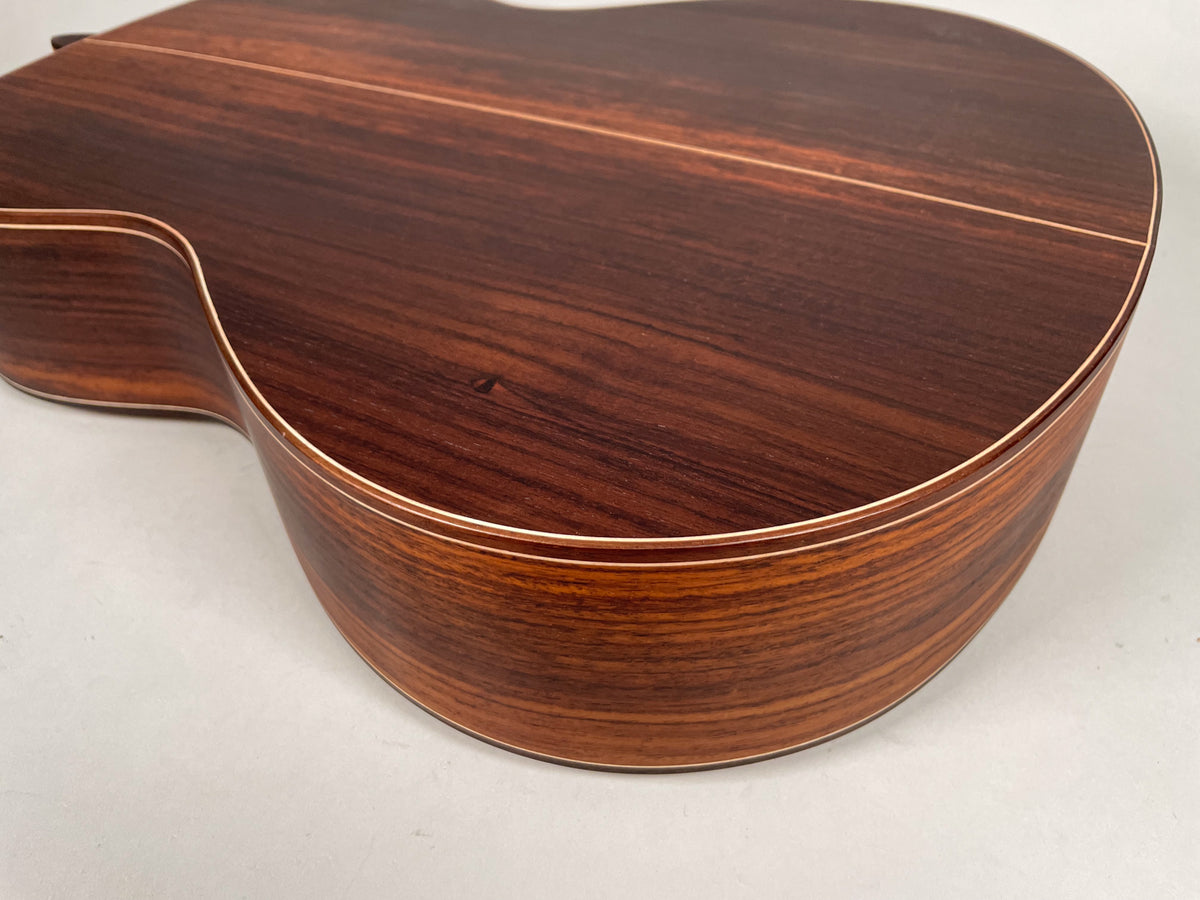 The lower bout of the dark reddish-brown acoustic guitar, showing the wood grain and light binding along the curved edges.