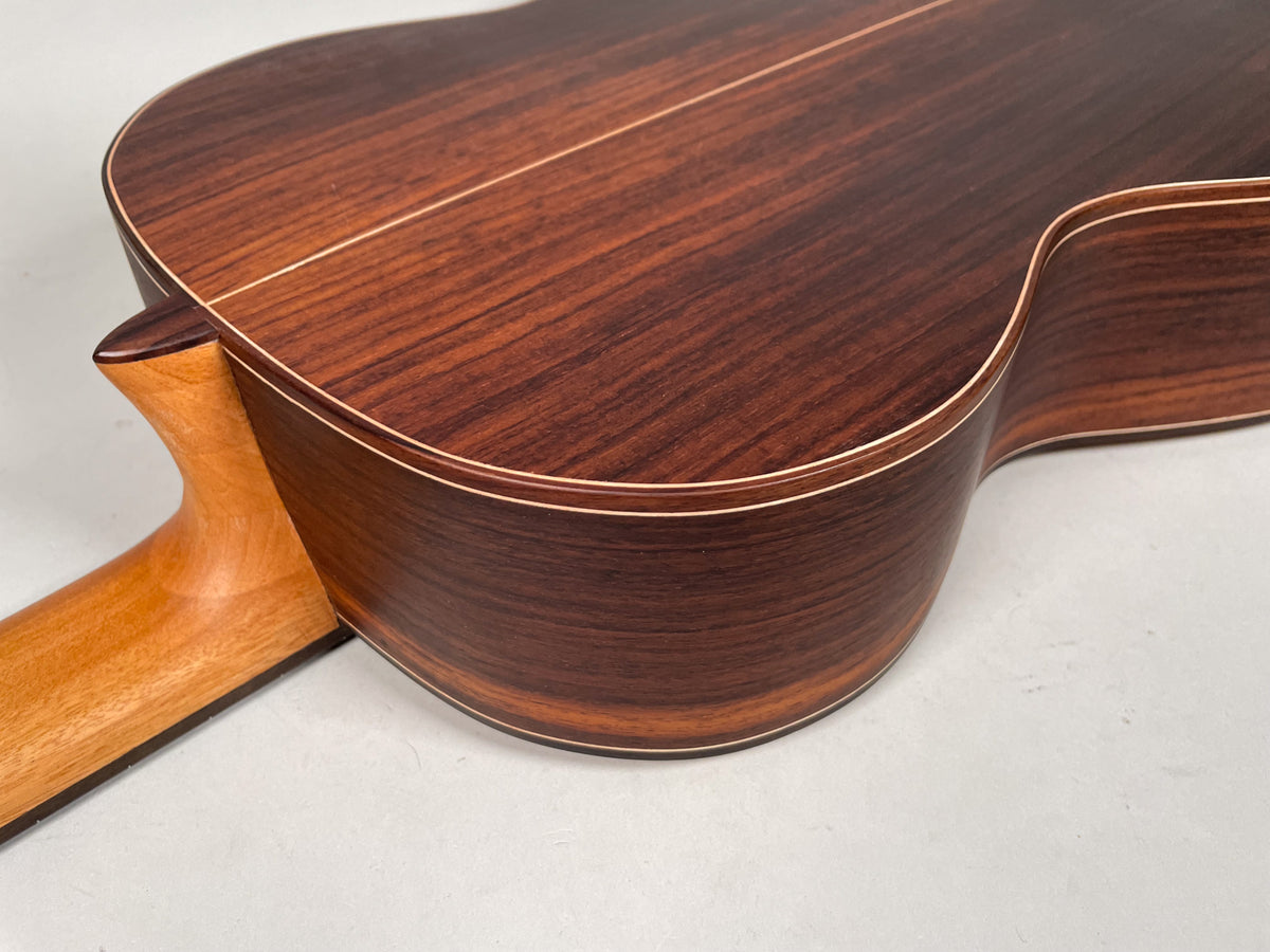 The guitar's dark reddish-brown back and side are framed from above, showing light wood binding and a light brown neck heel.