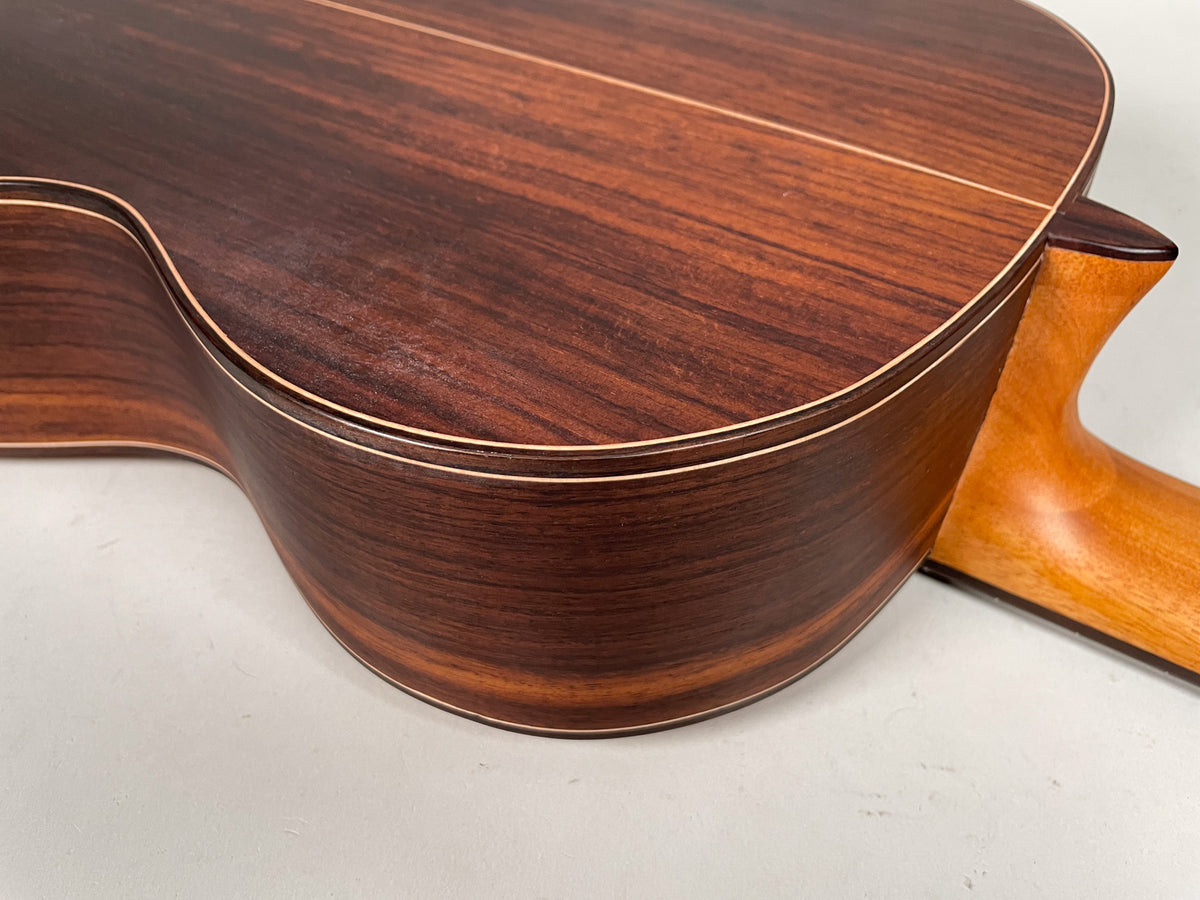 Close-up of the guitar's dark reddish-brown wood back and side, with light binding and a natural-colored neck heel.