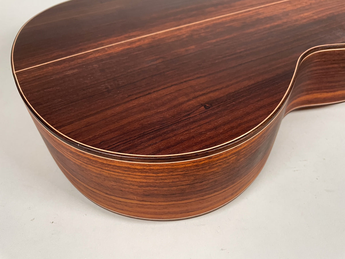 Close-up of the lower bout and waist of the dark brown, glossy guitar body, showing wood grain and light binding.