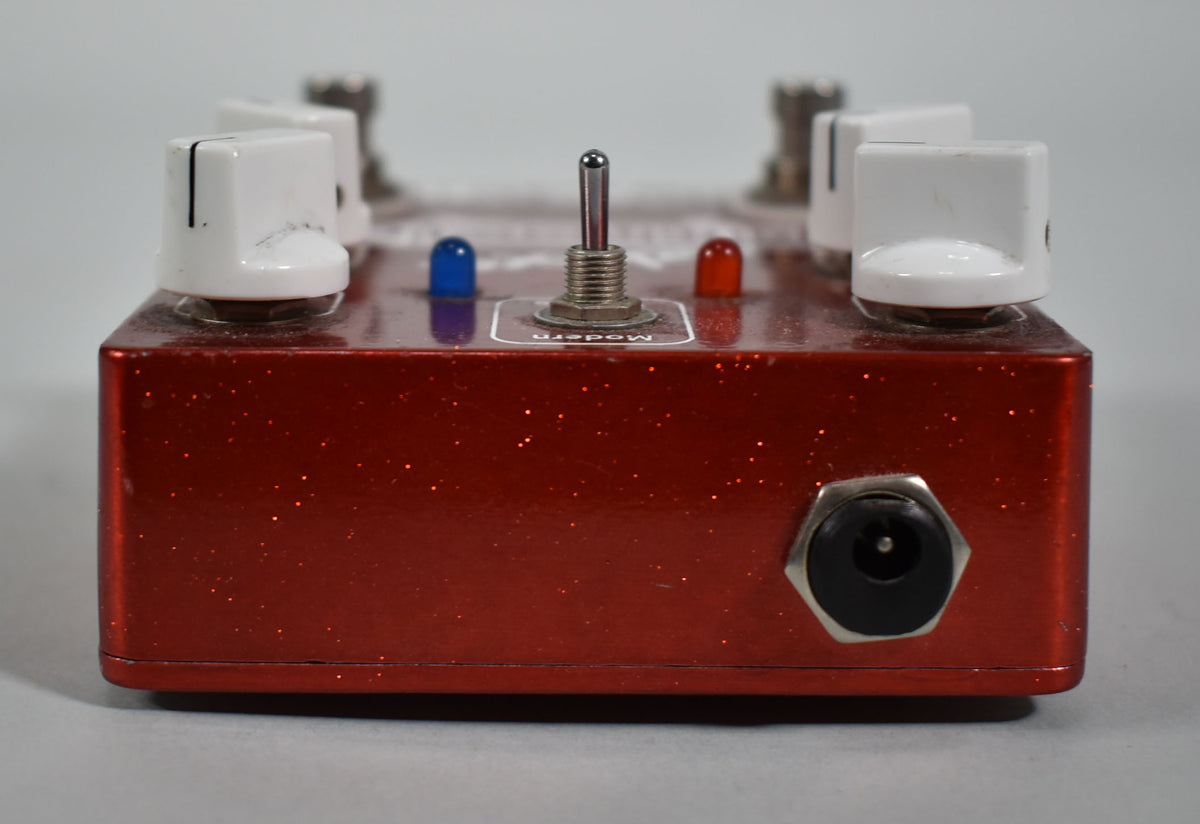 A red glitter guitar pedal with white knobs, a metal toggle switch, blue and red LEDs, and a power input jack.