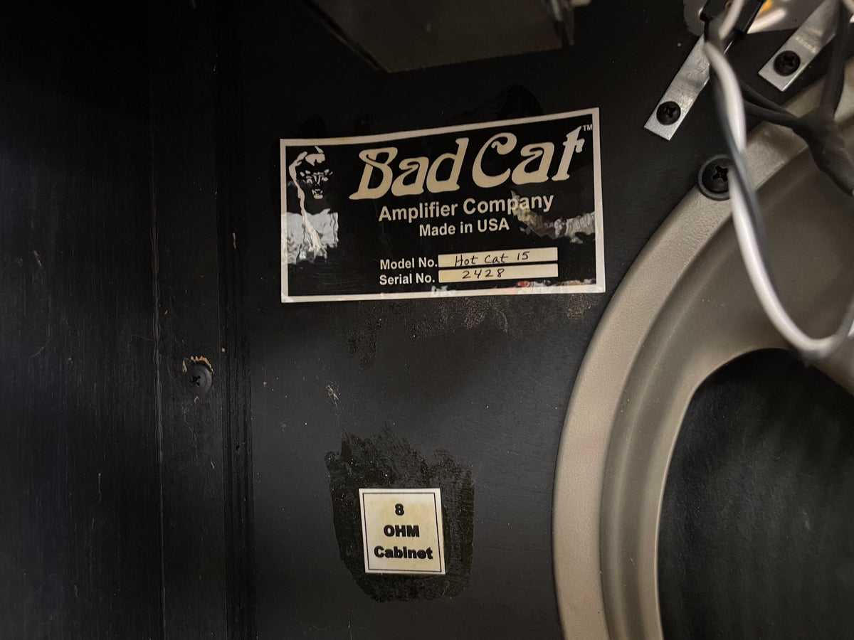 The amp's black interior with a white label showing "Hot Cat 15" and "2428", an 8 OHM label, and a speaker frame.