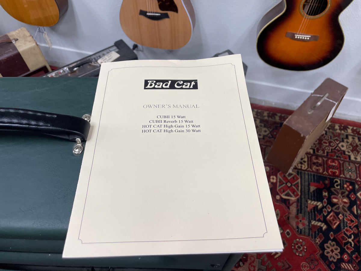 The amp's dark green tolex top and black leather handle are visible, with an owner's manual covering most of the frame.