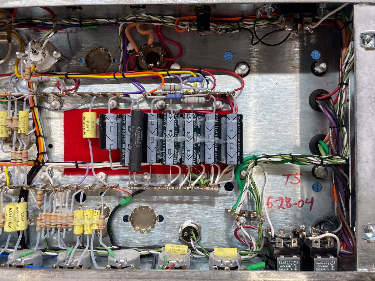 Overhead view of the amp's internal wiring, showing numerous capacitors, resistors, and colorful wires on a silver chassis.