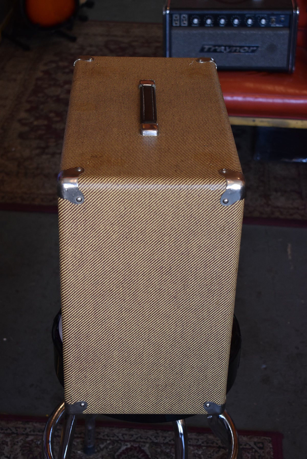 Top-down view of the tweed-covered cabinet, showing the brown leather handle and four shiny metal corner protectors.